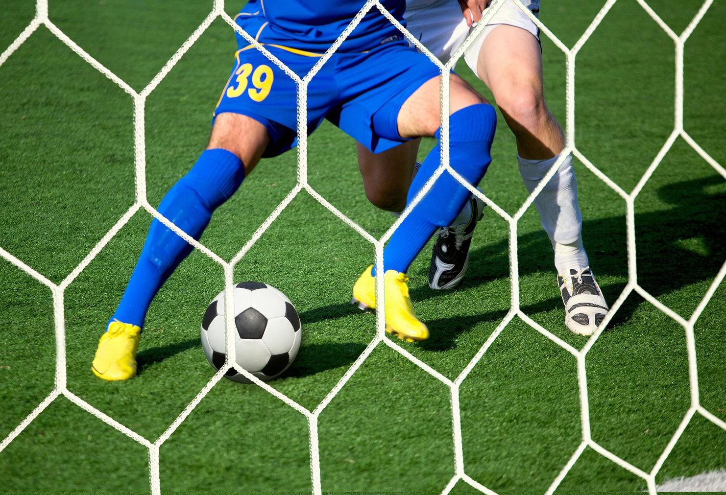 Zwei Fußballspieler in blauen und weißen Trikots kämpfen um einen Fußball vor einem Tor mit Netz.